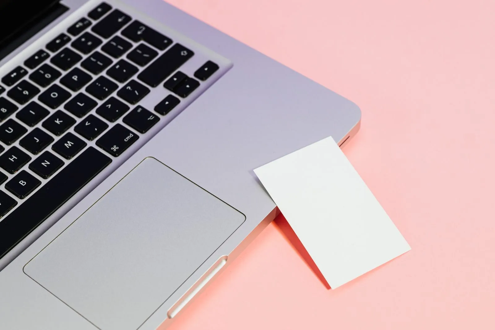 Close-up of a laptop with a blank card on a pink background, ideal for tech concepts.